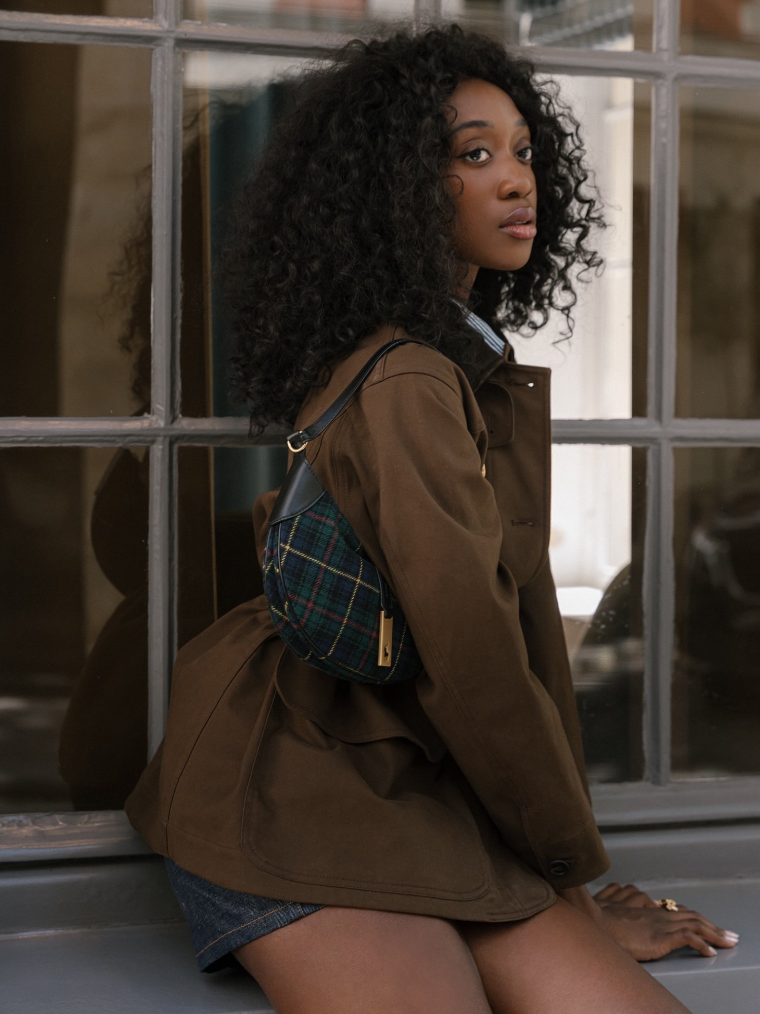 Emmanuelle Koffi with defined curls wearing a cropped trench coat and Ralph Lauren bag.