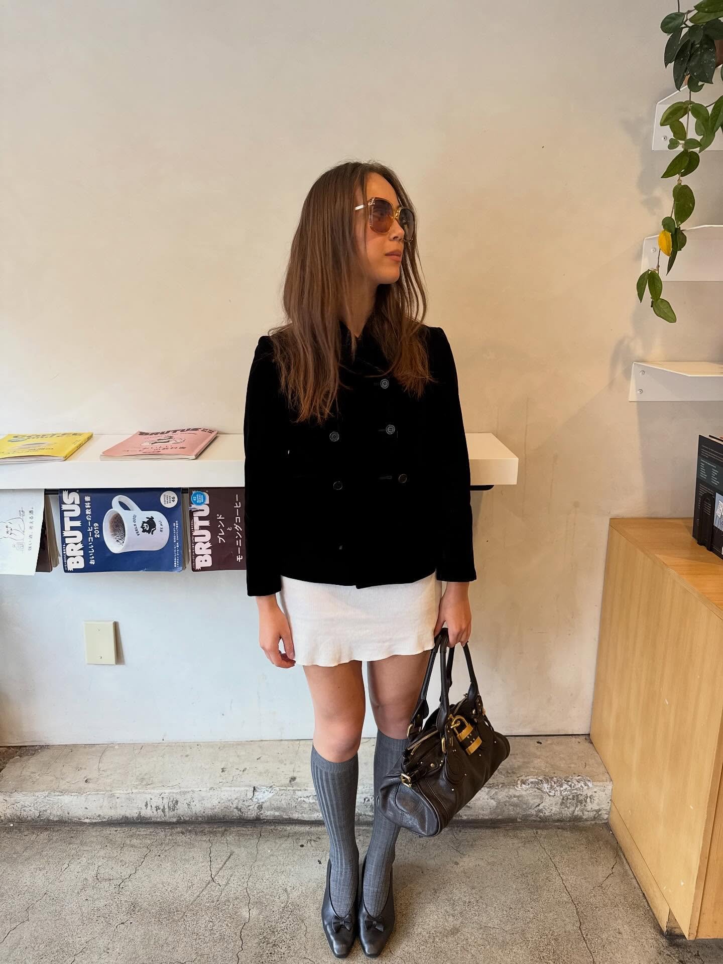 Laufey is wearing a double-breasted coat, a white mini skirt, knee-high grey socks, pumps, and a Chloé Paddington bag