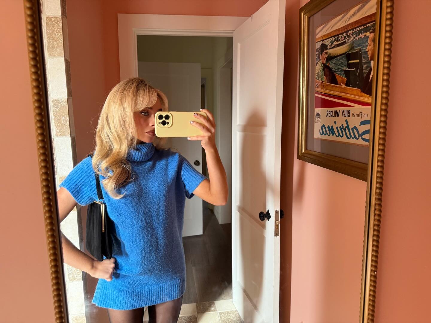 Sabrina Carpenter is wearing a cobalt blue sweater dress, tights, and a vintage purse