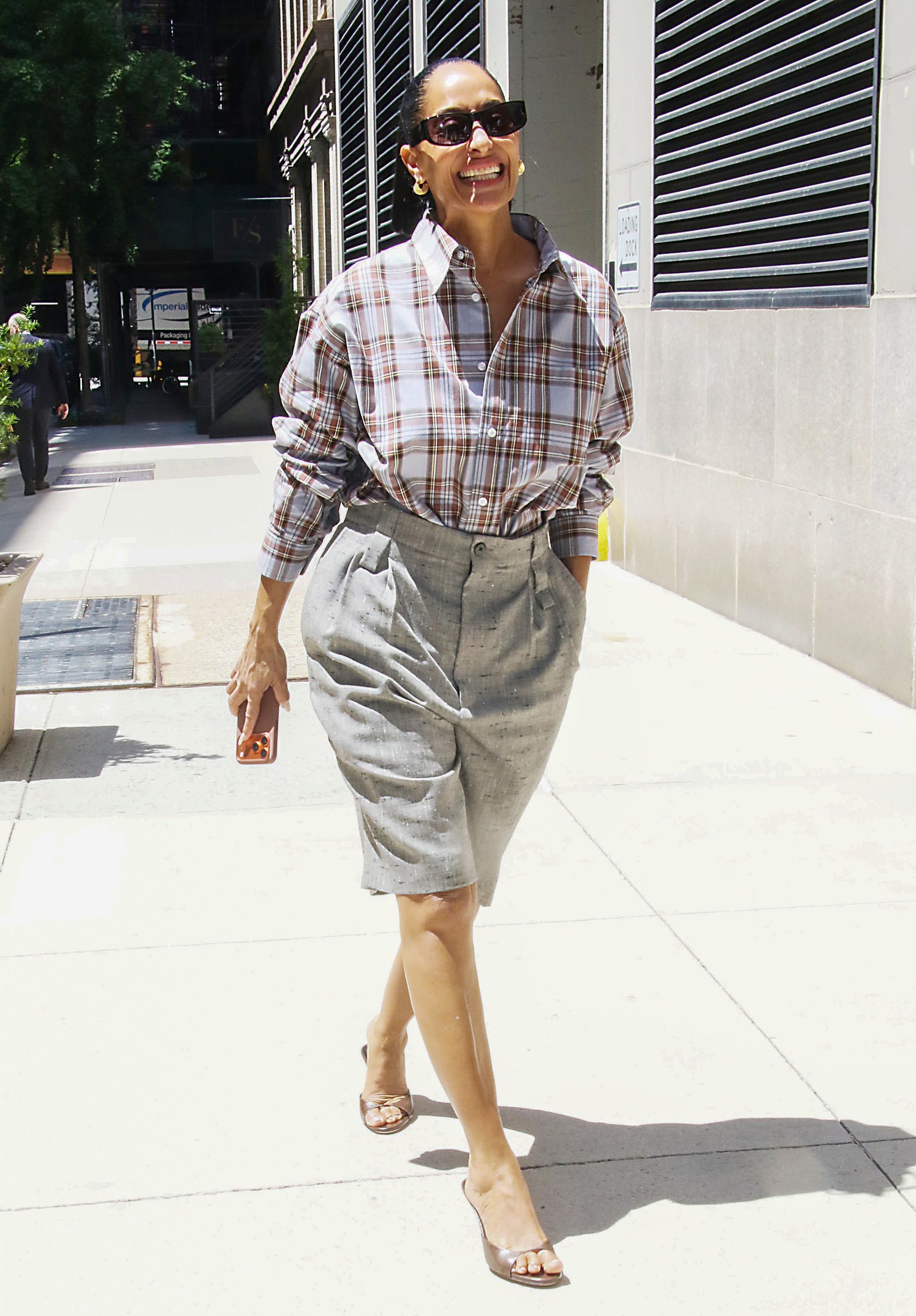 Tracee Ellis Ross wears Bermuda shorts with brown peep-toe mules and a checked shirt.